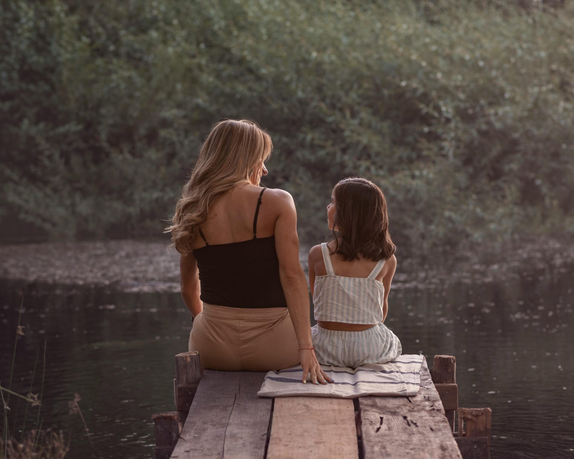 A loving moment between mother and daughter sitting on a pier at sunset.