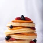 Tall stack of fluffy pancakes topped with blueberries, strawberries, and orange slices.