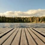 Serene wooden dock with a forested lake view under a bright summer sky in Sweden.