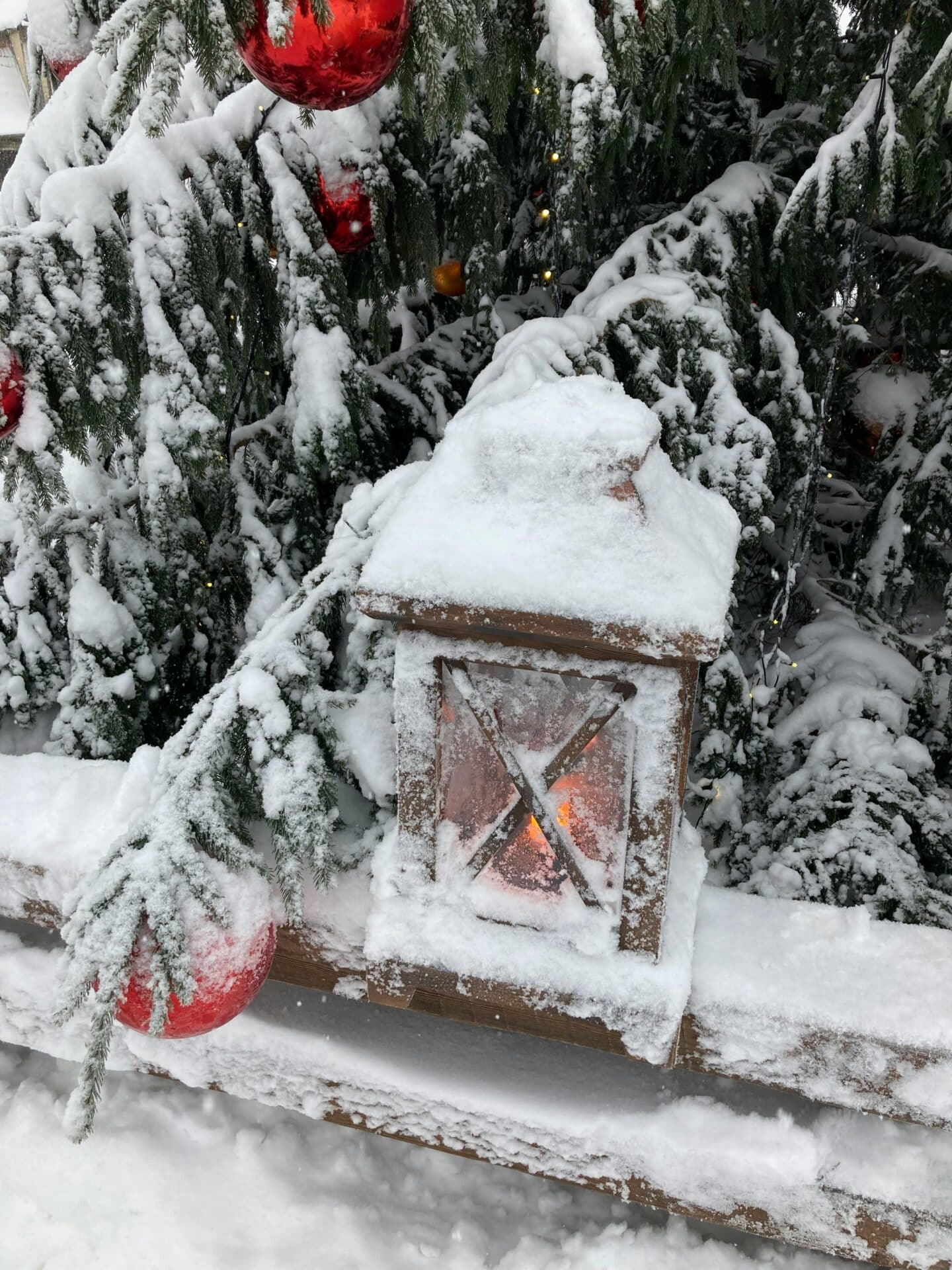 A festive winter scene with a snow-covered lantern and red ornaments on a pine tree.