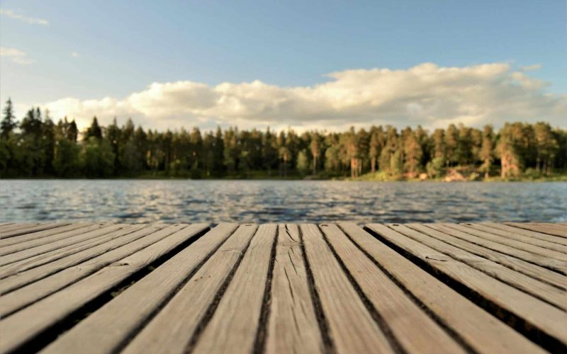Serene wooden dock with a forested lake view under a bright summer sky in Sweden.